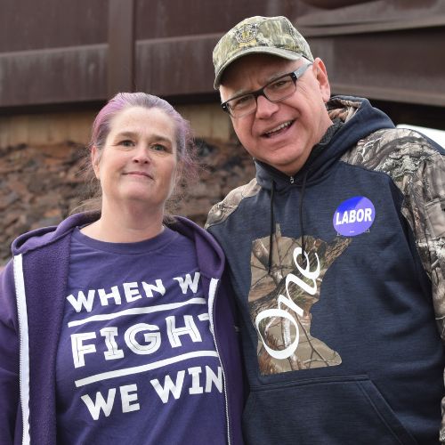 waltz wearing a labor sticker next to a woman wearing a shirt that says "When we fight we win"